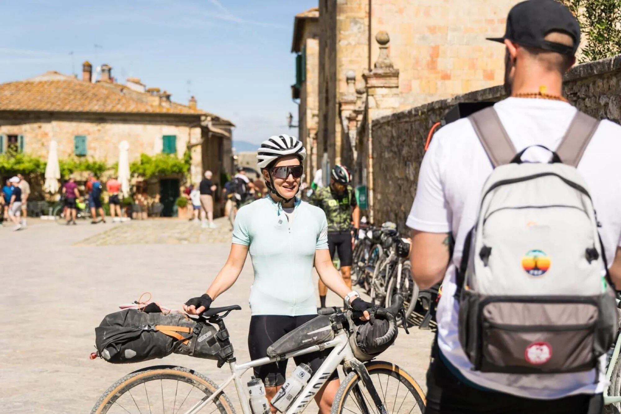 A rider with a gravel bike loaded with bikepacking bags in a Tuscan square
