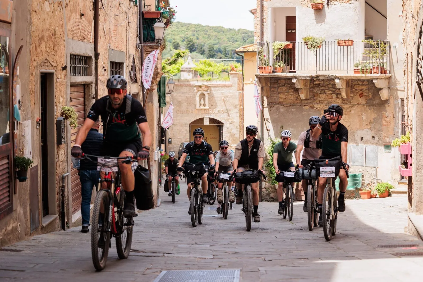 Un gruppo di ciclisti con le bici cariche attraversa un vicolo del borgo di Campiglia Marittima